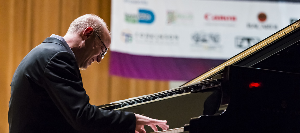 A man in a dark suit playing the piano on stage