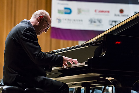 A man in a dark suit playing the piano on stage