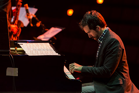 Man in a dark suit looking down as he is playing the piano