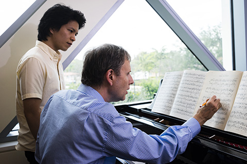 Instructor making notations on sheet music while a student musician looks on