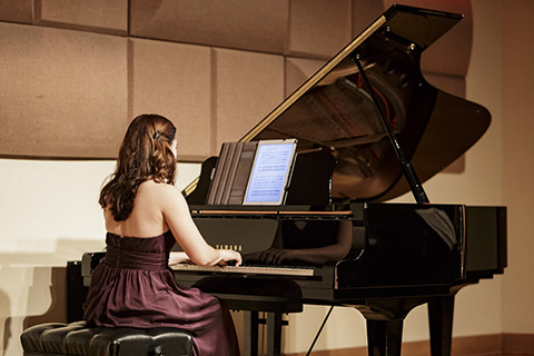 Woman in a red dress sitting down and playing the piano