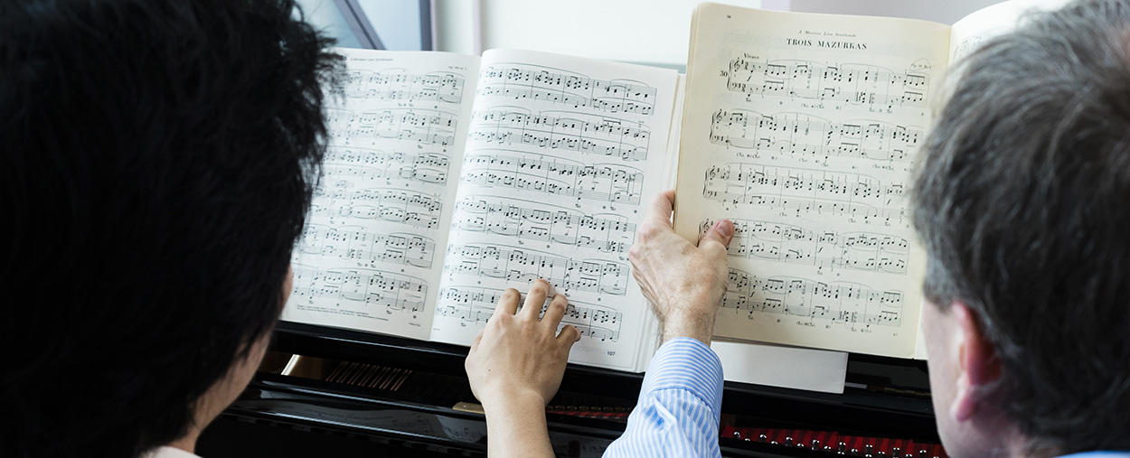 Two people examine sheet music resting on a piano